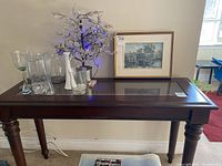 Full front view of dark wood console table with glass top and cane detailing beneath the glass, displaying decorative items on top.