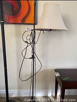 Full view of iron floor lamp showing off white bell-shaped fabric lampshade and black iron frame with electrical cord wrapped around stand