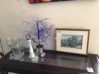 Overall view of the framed print, bonsai tree, and six glass vases on a dark surface beneath a wall painting