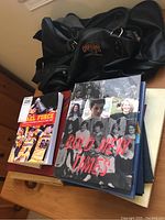 Black leather Queen's football duffle bag and several yearbooks on wooden table.