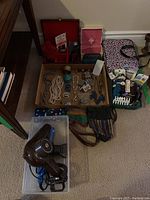 Overview of assorted costume jewelry, vintage hair dryer, makeup bag, small wallets, and storage boxes taken inside a room.