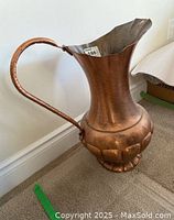 Full view of large decorative copper pitcher with bulbous embossed base and tall flared neck.