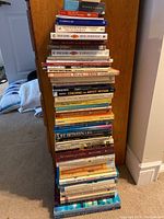 Stack of 30 mindfulness and meditation related books leaning against a wooden wall in a home setting.