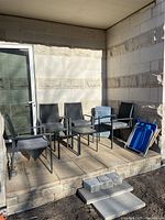 Photo of 4 steel patio chairs with mesh seats and backs, 2 tables with glass tops, folding beach chair and storage bin on a stone patio.