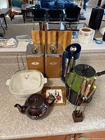Wide shot showing all items on countertop including canisters, fondue pot with forks, cutting board, teapot, Corning Ware dish, coffee carafe and tile