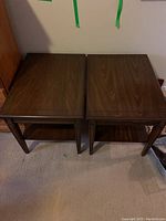 Top view of a pair of dark stained solid wood side tables placed side by side, showing mainly the tabletops and part of the shelves below.