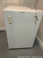 View of the white Kenmore small freezer, showing the front door, handle, and power cord on top.