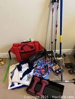 Overview of the lot showing red carrying bag, under desk pedal exerciser, pair of adjustable walking sticks, dumbbells, padded seat, curling broom, and iron meditation balls on floor.