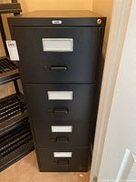 Front view of closed black steel 4-drawer legal filing cabinet with label holders and handles visible