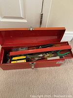 Photo showing open red metal toolbox with various hand tools in storage tray