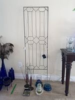 Full view of metal trellis leaning against wall, various candle holders and coasters arranged on floor beside a wooden table