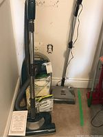 Kenmore canister vacuum with hose, wand, and vacuum filter bags stacked beside it against a wall.