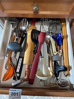Drawer containing a variety of kitchen utensils such as spoons, spatulas, ladle, rolling pin, potato masher, and other cooking tools.