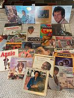 Photo showing an assortment of vinyl record covers including Christmas, disco, country, and soundtrack themes spread on a surface.