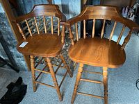 Two oak swivel barrel back bar stools side by side on a concrete floor.