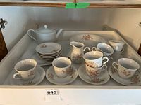 Top view of the tea set pieces arranged in a drawer showing cups, saucers, creamer, teapot, serving bowl, and platter with floral pattern.