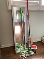 Swiffer mops, Vileda telescopic mop, behind-the-door mirror, and extra mop pads arranged against a wall below window.