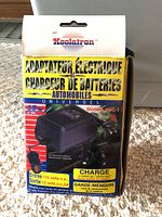 Boxed Koolatron battery charger labeled 'Adaptateur Electrique Chargeur de Batteries Automobiles' Model ABC-1, showing front packaging with specifications and voltage info.