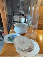 Image showing ceramic decorative plates with scenic and commemorative prints alongside clear glass vases and a white ceramic container with lid