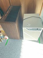 Two older style appliances side by side on grey carpet, one beige dehumidifier and one woodgrain humidifier