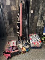 Full lot showing golf umbrellas, golf clubs, golf balls in plastic bins, golf shoes, golf training aids and booklets on the floor against wood background