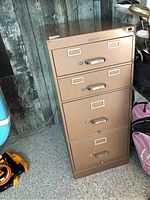 Front and slightly angled view of the brown metal filing cabinet showing all four drawers with silver handles and label holders.