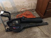 Full view of Toro Super Blower with attached blower tube and orange extension cord coiled beside it on concrete floor