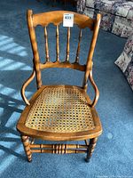 Front view of the wooden occasional chair showing cane seat and spindle backrest with some light shadow on the carpeted floor.