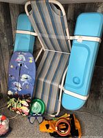 Photo of blue floating pool chair, boogie board with dolphin design, snorkel mask, and assorted pool floats and toys on carpet.