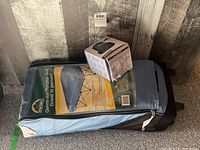 Blue storage bag containing the folded queen-size portable bed and the pump's original box on top.