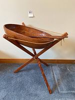Front view of large wooden salad bowl on wooden tripod stand with salad utensils resting across the top.
