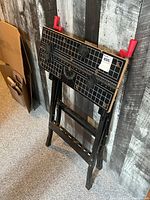 Foldable Jobmate saw horse workbench closed and leaning against wall.