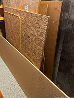 Eight pieces of scrap plywood leaning vertically against a wall. Pieces vary in size and appear partly rough with OSB texture and partly smooth plywood surfaces.