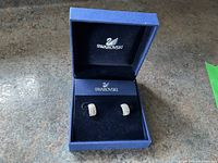 Swarovski earrings displayed inside blue Swarovski box with logo on lid and interior.