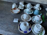 Eight vintage teacups placed upside down on their matching saucers on a floor surface for display. Visible floral patterns and some blue and gold designs.