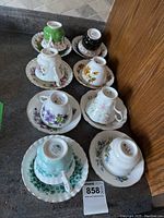 Eight teacups and saucers displayed on kitchen counter, showing various floral designs and colors