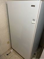 Full front view of white upright Kenmore freezer positioned in corner, showing size and power cord on floor.