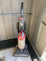 Front view of red and gray Bissell PowerLifter upright vacuum cleaner, showing dust container and hose attachment.