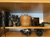 Wide shot showing shelf with binoculars, camera, film box, basket, tripod