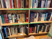 Two wooden shelves filled with various hardcover and paperback books of assorted sizes and colors, showing a mixed genre collection predominantly of history and fiction.