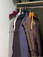 Photo of 7 coats and sweaters hanging on hangers in a closet, showing various colors and materials including gray, navy, brown, black, and blue.
