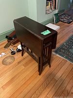 Side view of the folded drop leaf table showing its vertical slat design and condition of the wood surface.