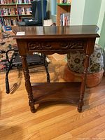 Solid walnut side table with carved drawer front and turned legs shown from front angle.