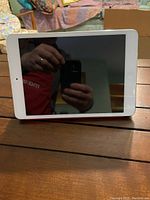 iPad with white bezel on black screen in red folding case on wooden table.
