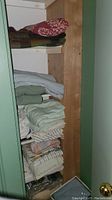 View of folded linens and a wool blanket on shelves in a small closet space.