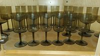 Seven smoked crystal white wine glasses in two rows on a wooden shelf.