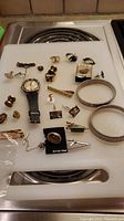 Overview of lot items including the watch, cufflinks, tie clips, pins, and rings on a white surface.