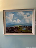 Full view of the framed painting showing the landscape scene with blue sky, clouds, hills, bushes, sheep, and pond.