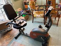 Side angled view of the recumbent exercise bike showing padded seat and backrest, control panel, and pedal setup.