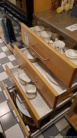 Wooden drawers open, shows multiple pieces of white china with gold trim.